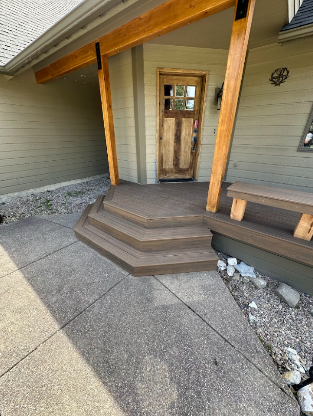 Entryway with steps, featuring a weathered wooden door and brown composite steps.  A concrete walkway leads to the steps.