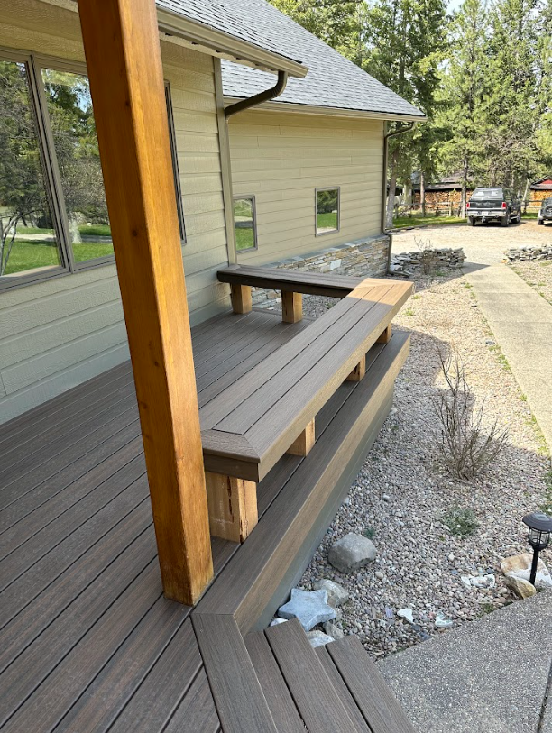 A wooden deck with composite benches and steps leading to a beige building. A brown pillar supports the roof.