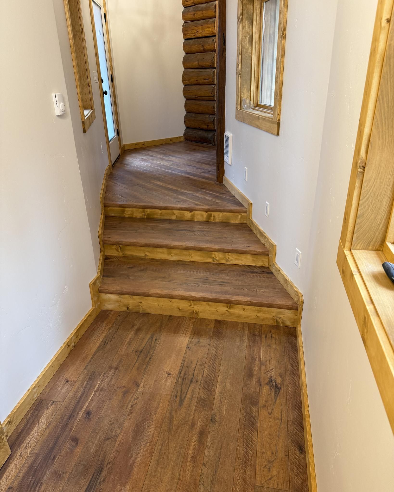 A narrow hallway with wooden stairs and flooring. The stairs lead upwards toward a staircase with wooden steps.