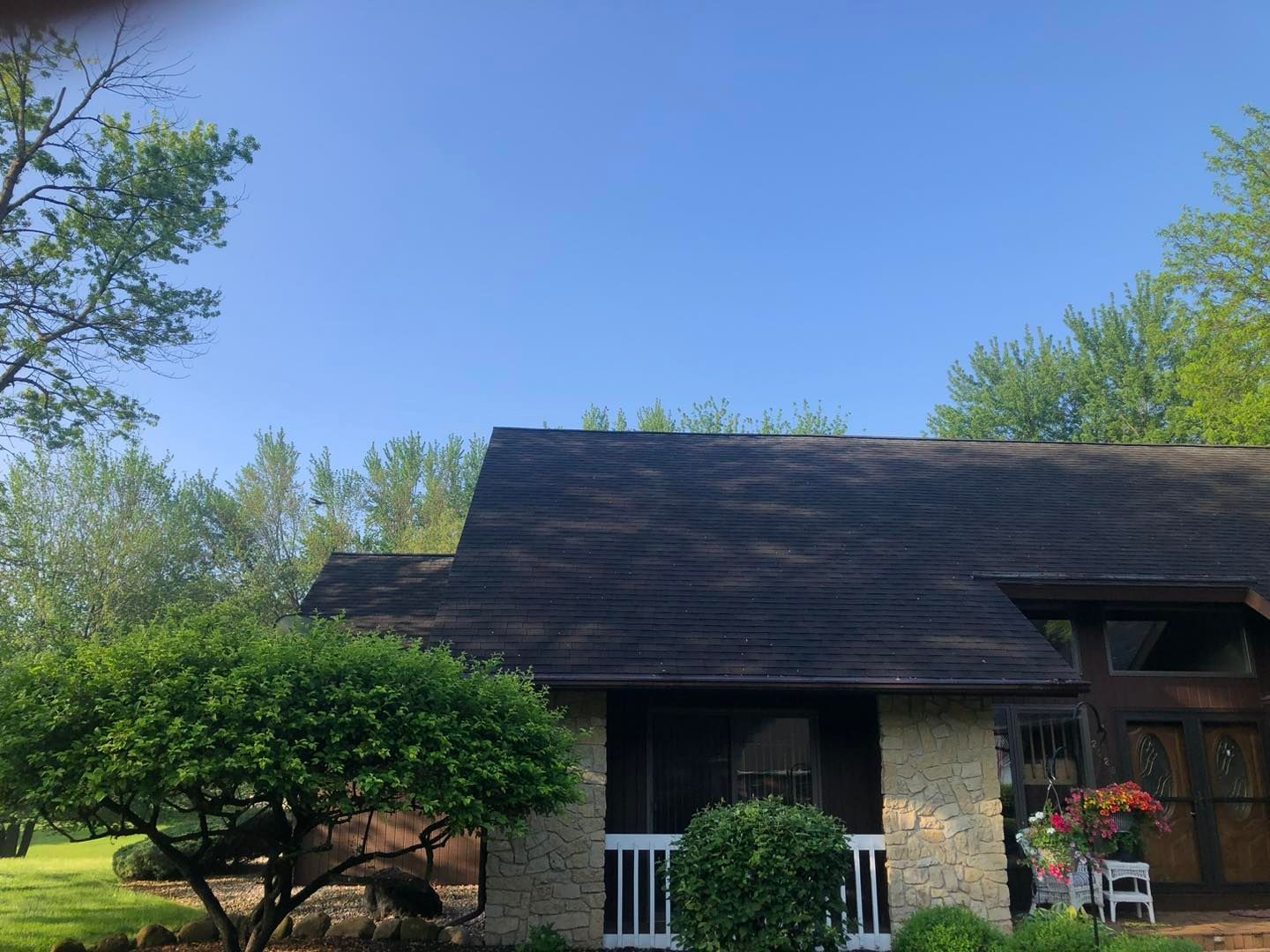 A house with a black roof is surrounded by trees and bushes on a sunny day.