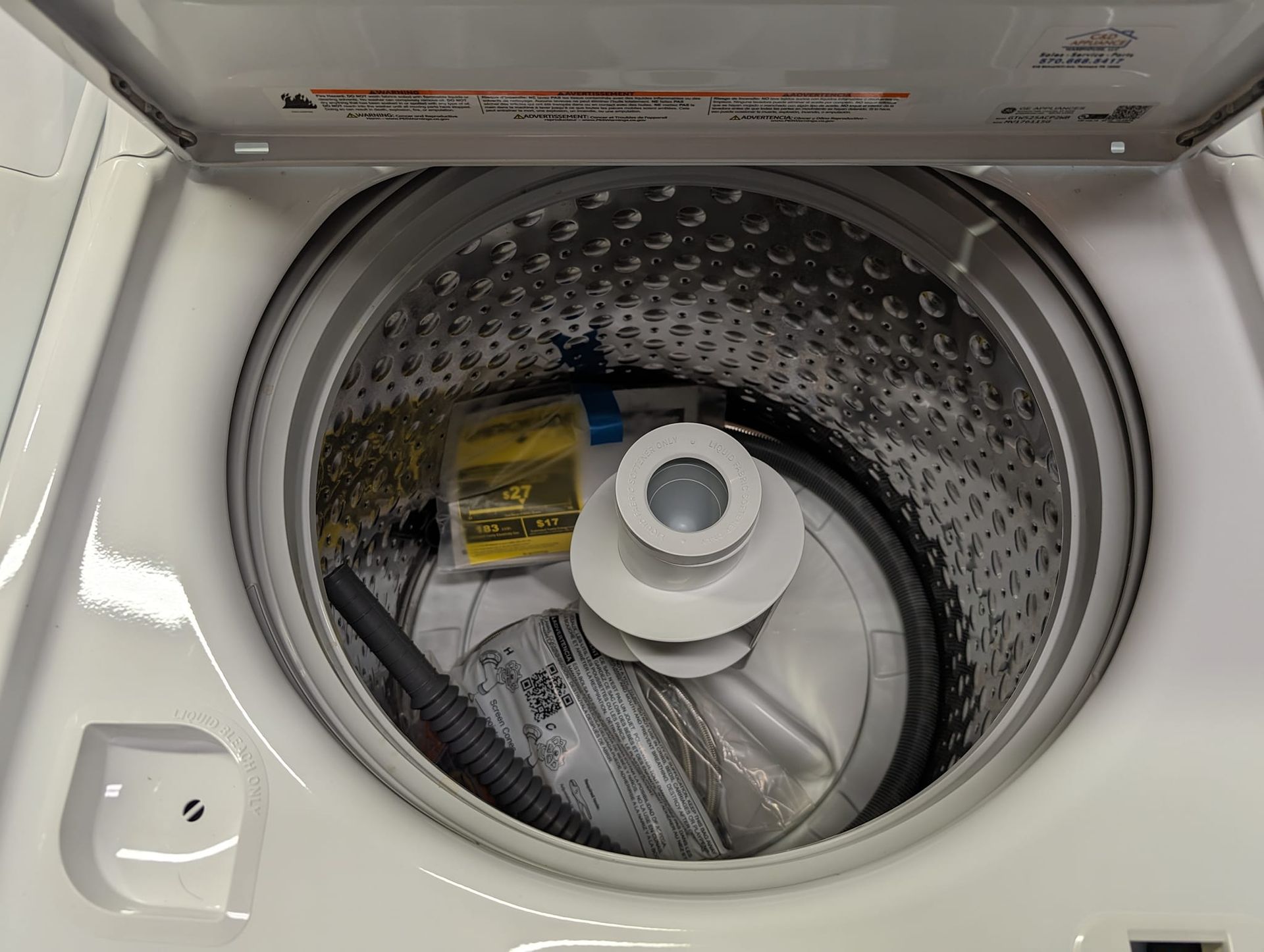 Open top-load washing machine. The stainless steel drum holds an installation kit.