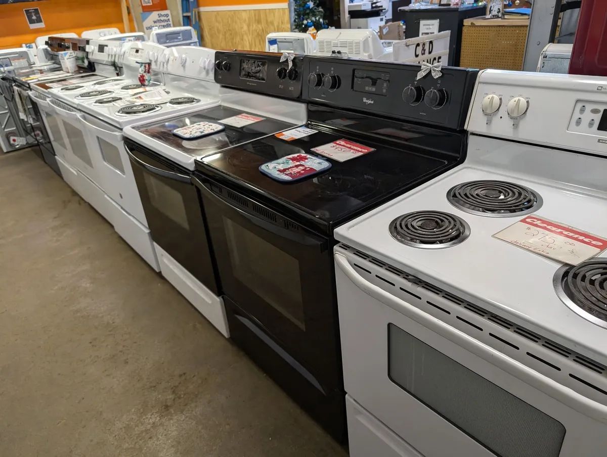 Row of white and black electric stoves on display in a store.