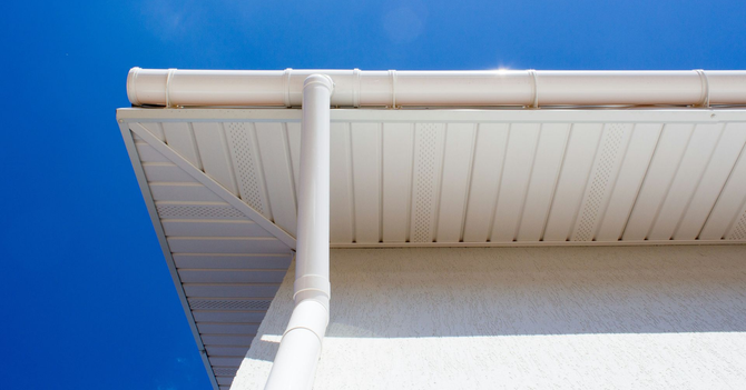 White house eave and rain gutter against a bright blue sky