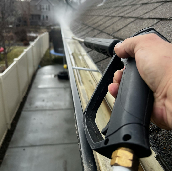 Hand holding a pressure washer spraying a rooftop gutter with water runoff below