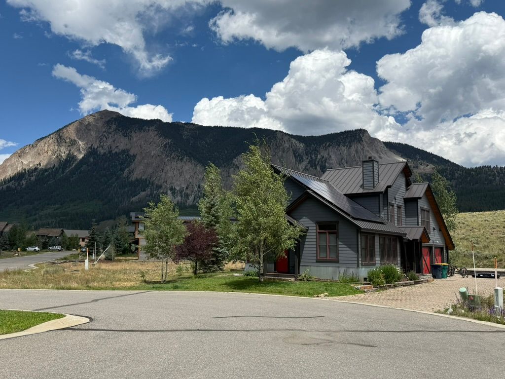 Gray house at the base of a mountain with puffy clouds.