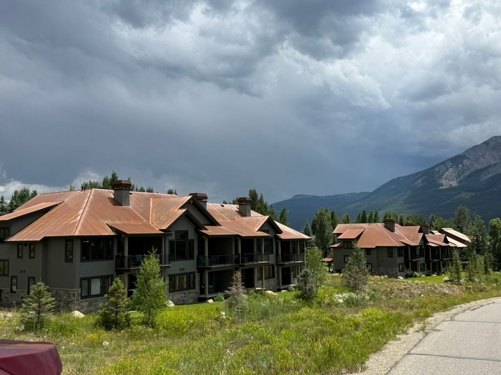 Apartment buildings with rust-colored roofs sit in a mountain landscape under a cloudy sky.