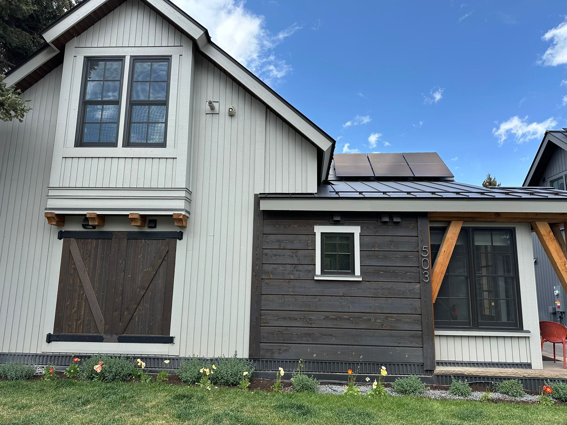 White house with dark wood barn door and brown extension. Solar panels on roof.