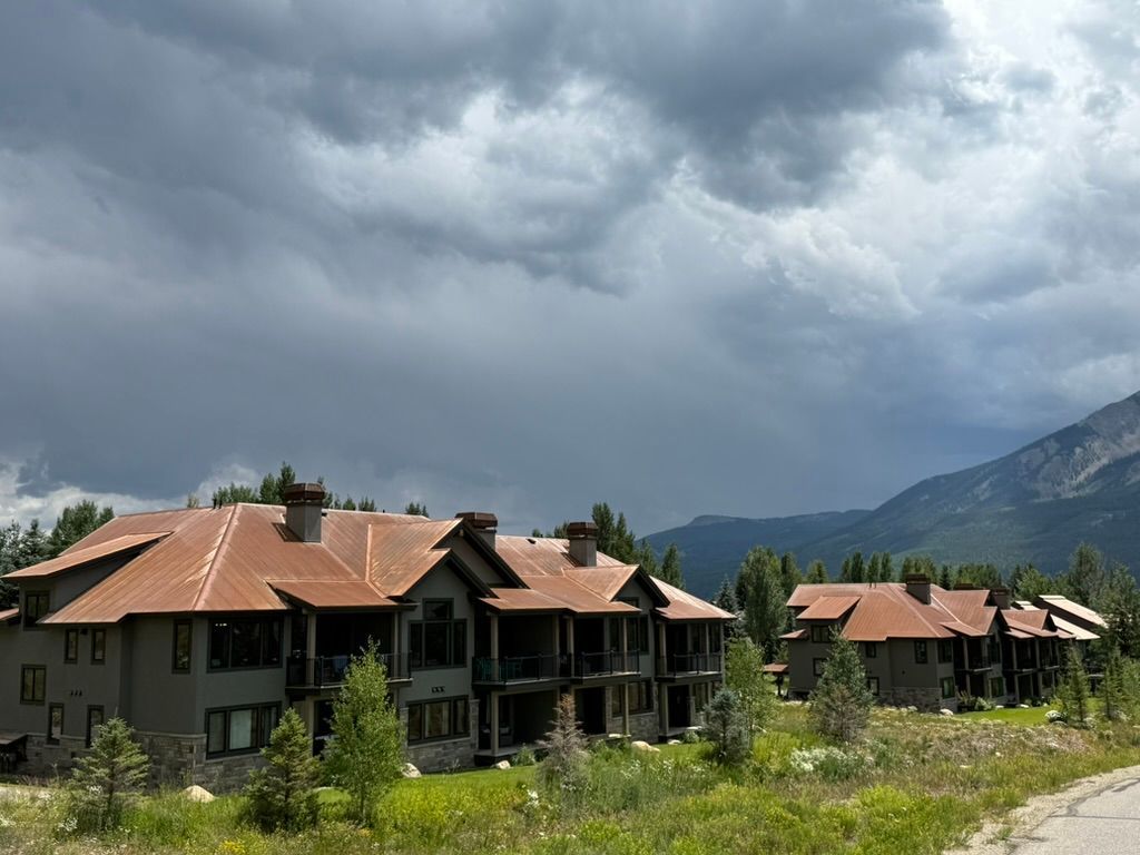 Condos with brown roofs nestled in a mountain setting under a stormy sky.