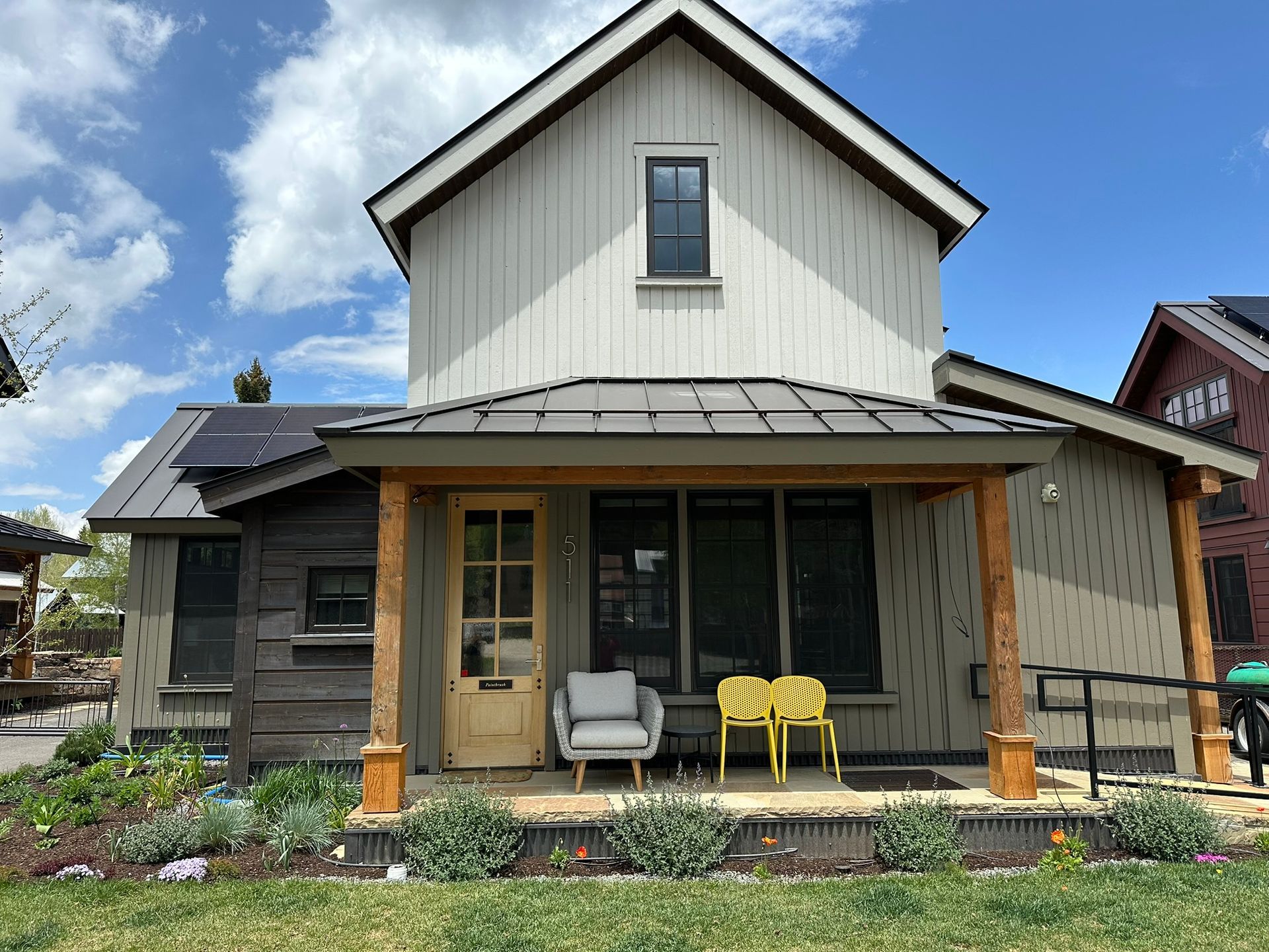Tan house with a porch and two yellow chairs, grey walls, and blue sky.