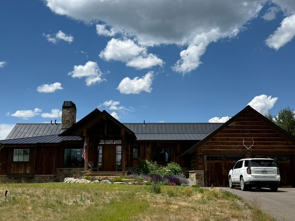 Rustic brown house with a dark roof, parked SUV, and a cloudy blue sky.