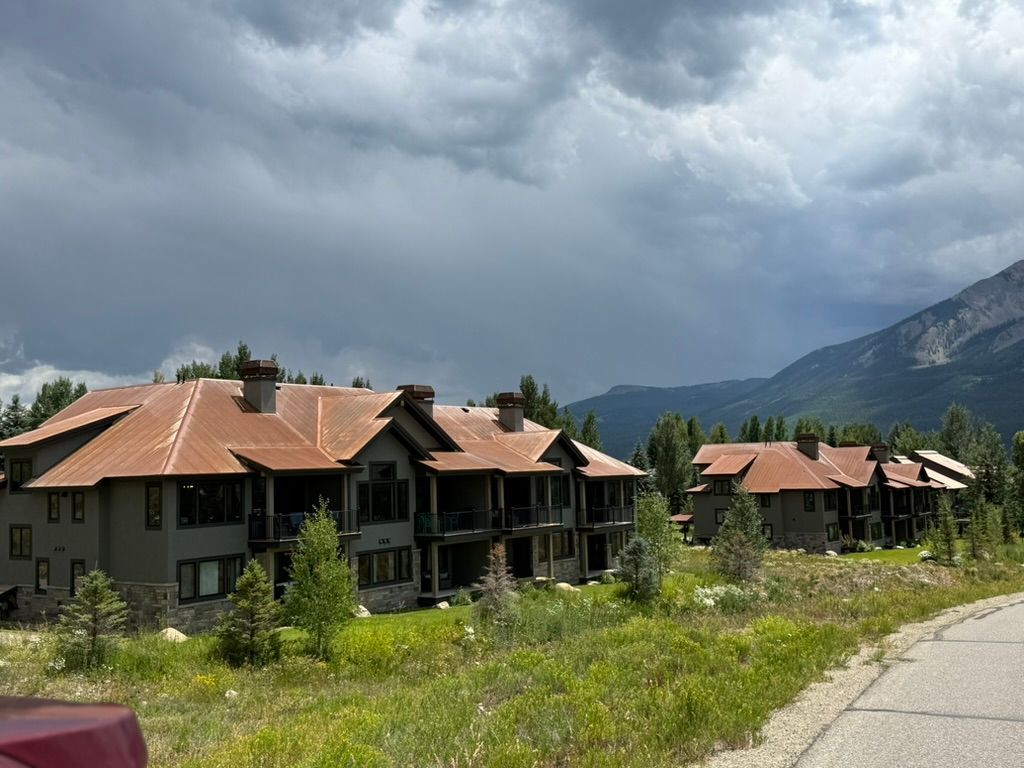 Condos with brown roofs, gray exteriors, set in a mountain landscape under a cloudy sky.