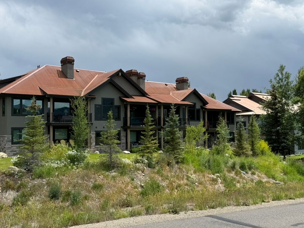Multi-story condo building with reddish-brown roof and green exterior in a mountainous setting.