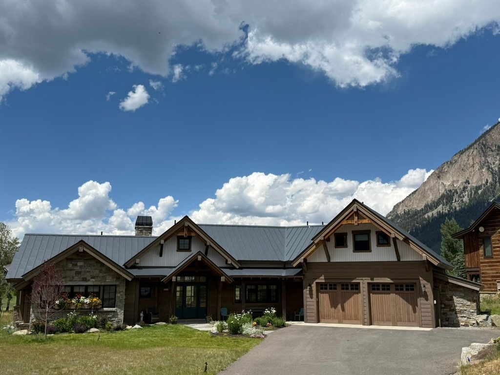 Mountain home with stone and wood exterior, two-car garage, and driveway on a sunny day.