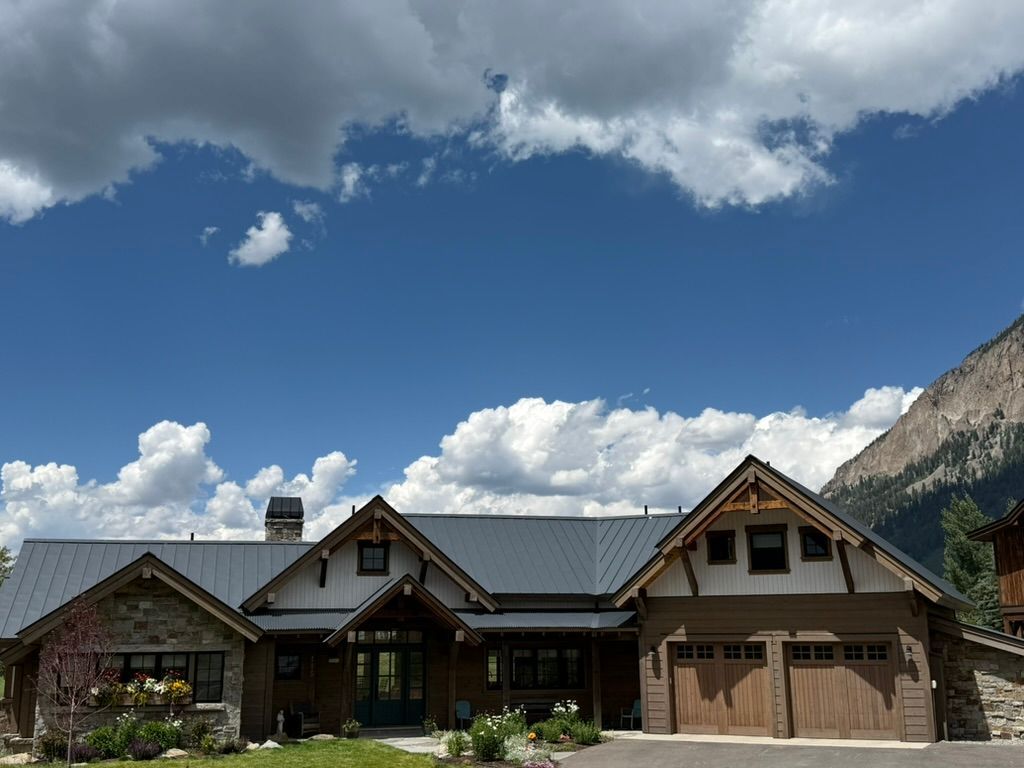 Mountain home with a gray roof, stone and wood accents, and a blue sky with puffy clouds.