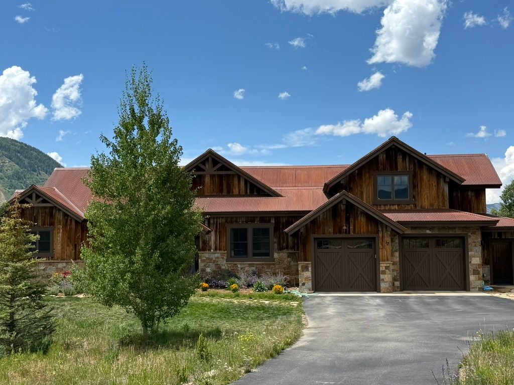 Rustic, wooden house with a red roof and two-car garage on a sunny day with a blue sky.