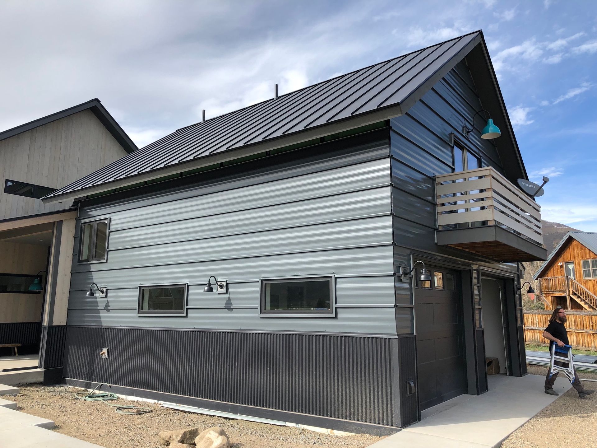 Modern two-story building with gray metal siding and a black metal roof, a balcony, and two garage doors.
