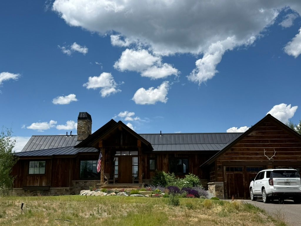 Rustic wood home under a blue sky with puffy white clouds; a white SUV is parked in the driveway.