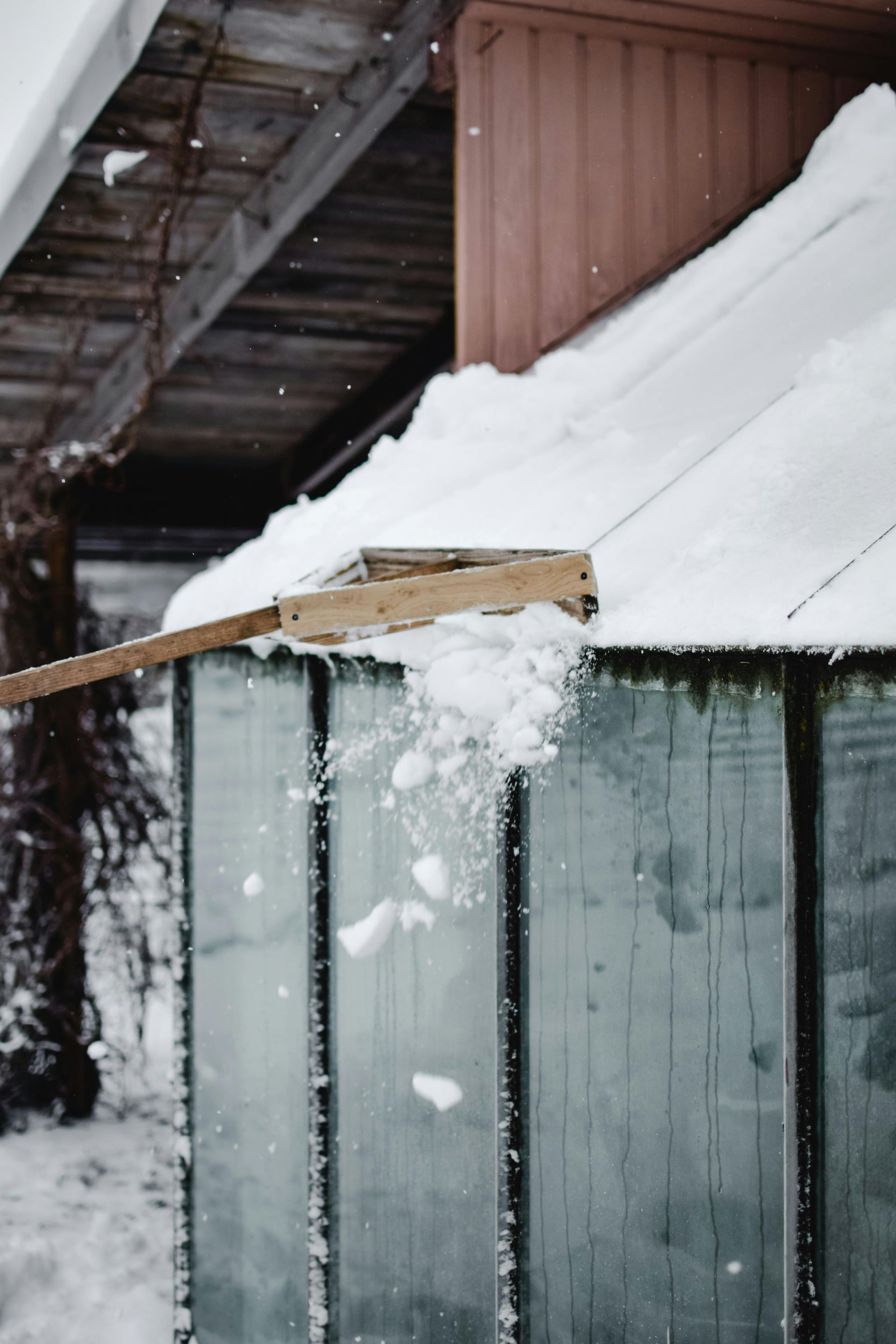 A snow shovel is being used to remove snow from the roof of a greenhouse