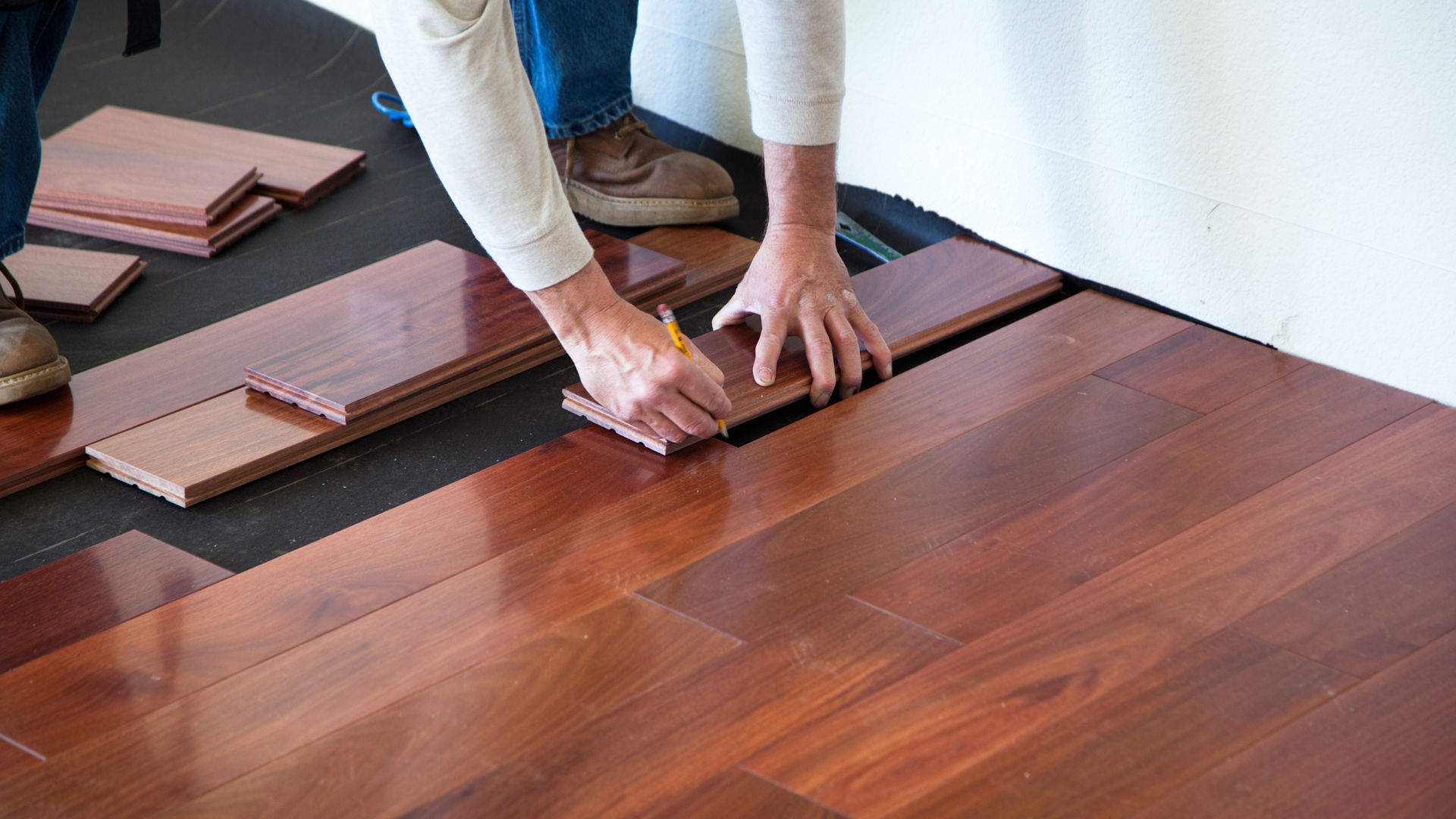 A person is measuring a piece of wood on a hardwood floor.