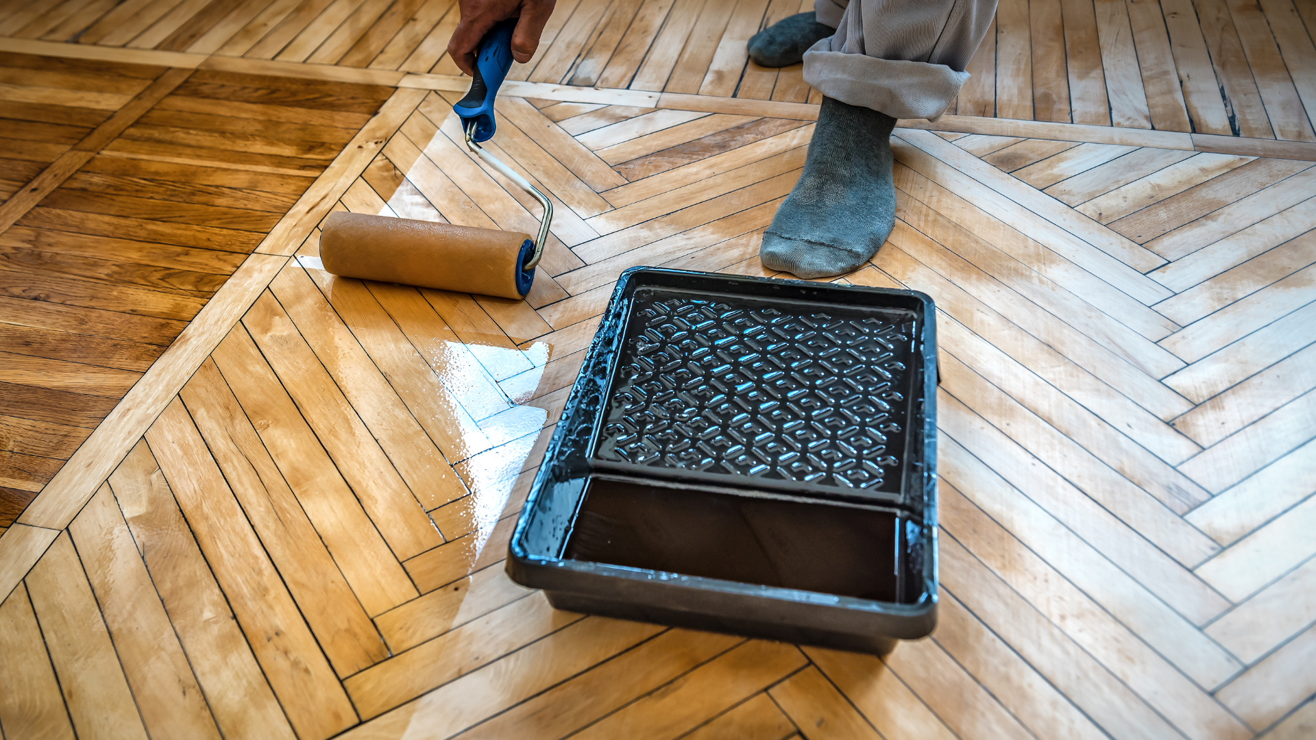 A person is painting a wooden floor with a roller.