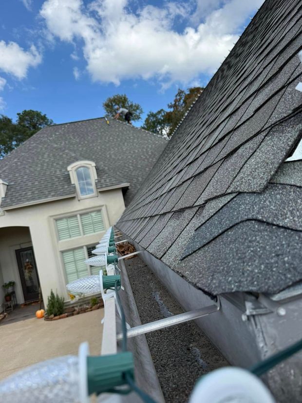 A gutter filled with debris on a house roof. Person on roof. Bright sky.