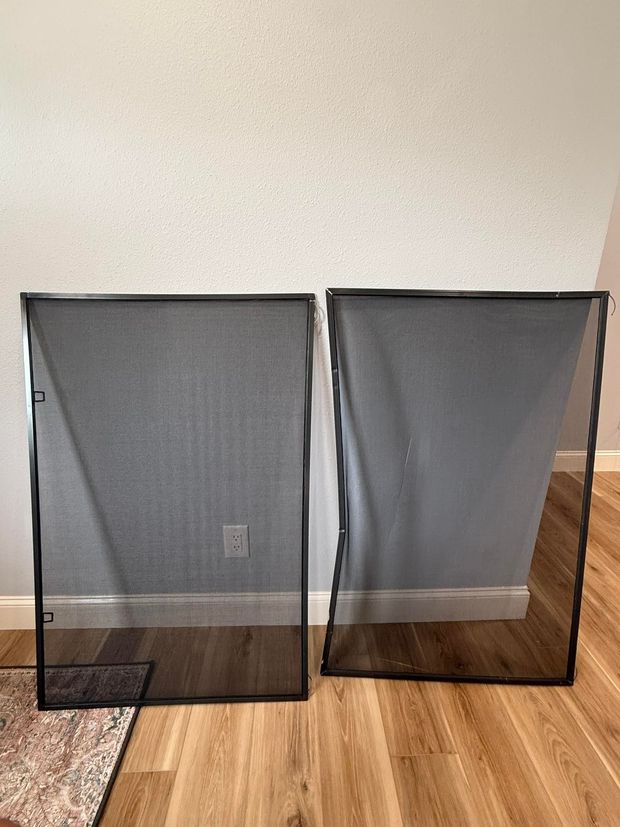 Two black mesh fireplace screens on a wooden floor, against a light gray wall.