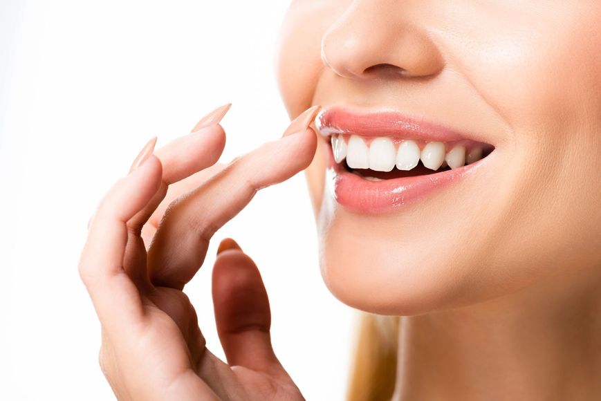 Primer plano de una persona sonriente sosteniendo un alineador transparente cerca de sus dientes.