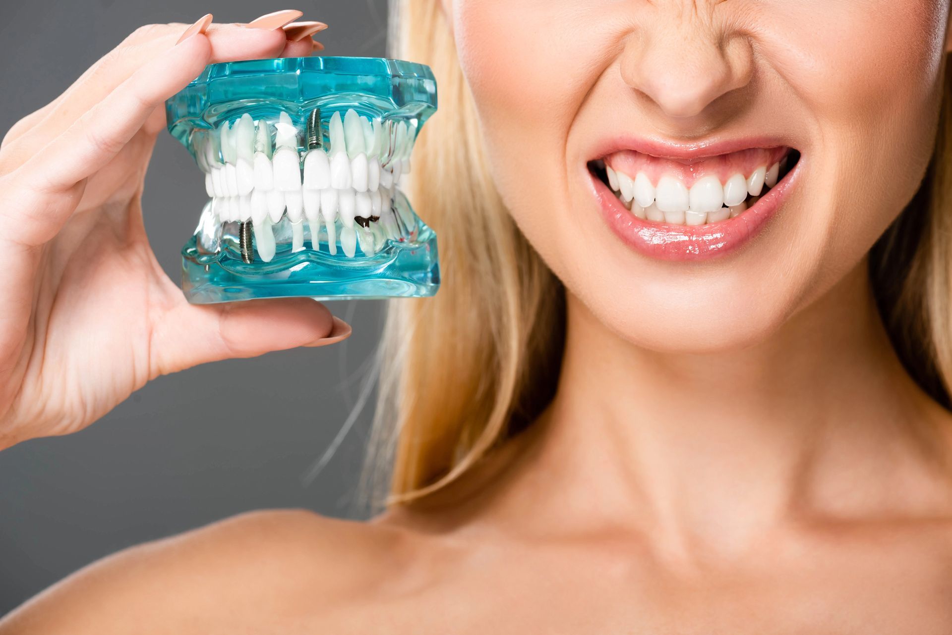 Mujer sosteniendo aparatos dentales transparentes y sonriendo con los dientes al descubierto.