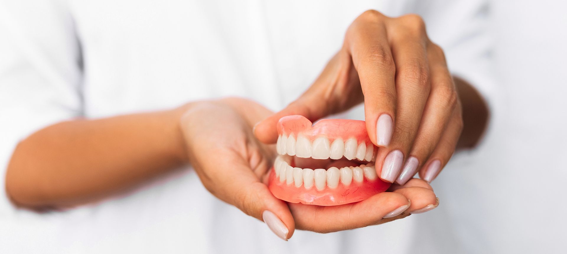 Manos sosteniendo una dentadura postiza removible sobre un fondo blanco.