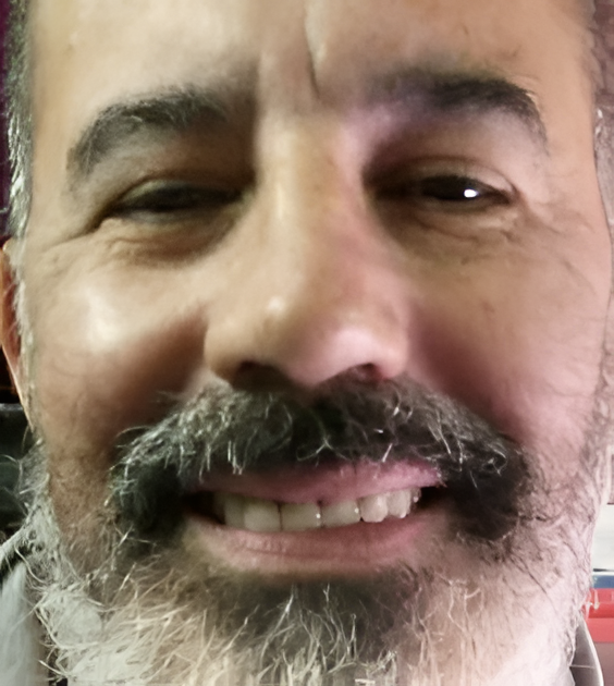 Primer plano de un hombre sonriente con barba y bigote canosos.