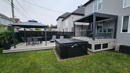 Terrasse moderne dans un jardin avec mobilier de jardin noir, gazebo et barbecue, à côté d'une maison et d'une pelouse.