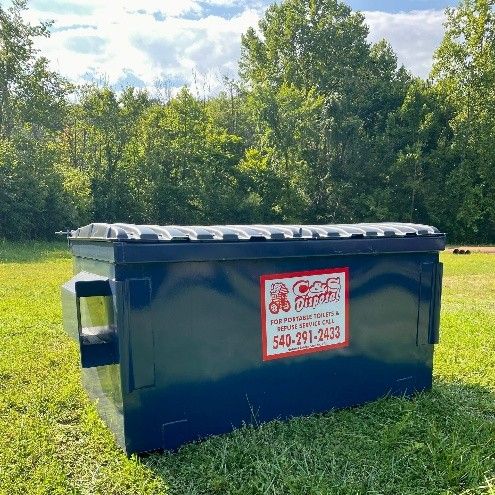 A large black roll-off dumpster placed on a grassy lawn and trees behind.