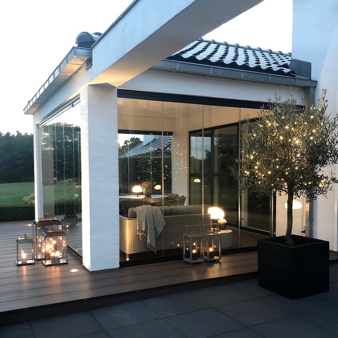 Patio moderno con pareti in vetro, colonne bianche e lanterne che illuminano la calda atmosfera del crepuscolo.