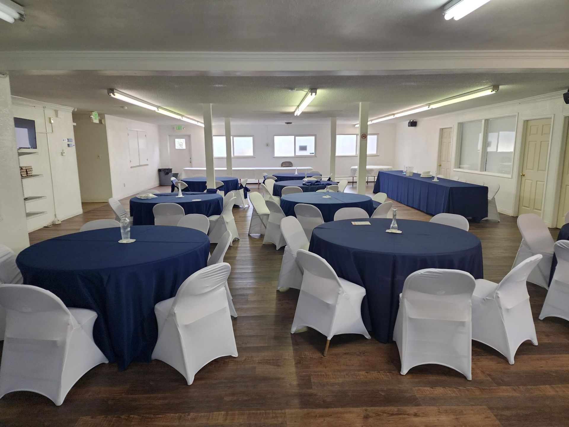 Conference room with round tables covered in blue cloths, white chairs, and wood floors.