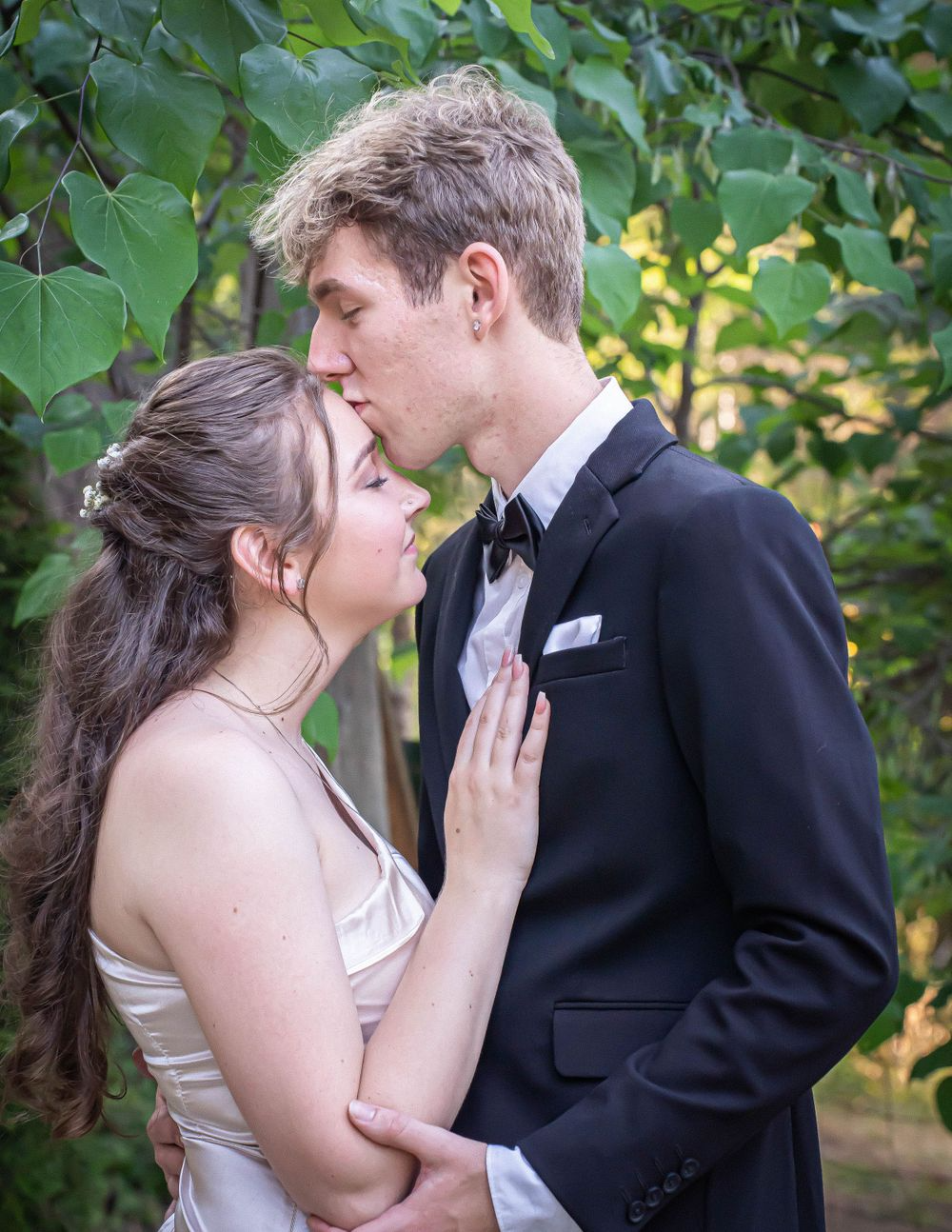 A bride and groom are kissing in front of a tree.