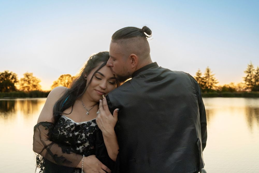 A man is kissing a woman on the forehead while standing next to a lake. A man is kissing a woman on the forehead while standing next to a lake.
