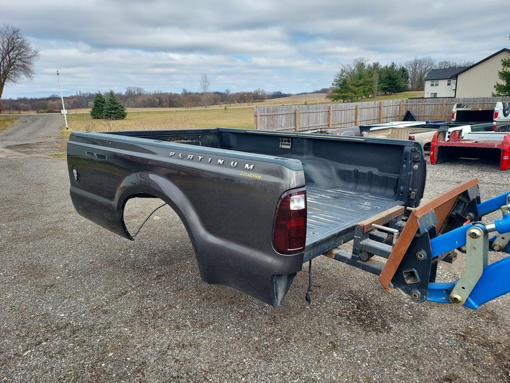A truck bed is sitting on the ground in a gravel lot.