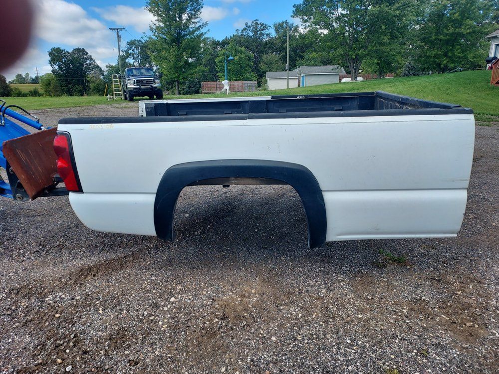 A white truck bed is sitting on a gravel road.