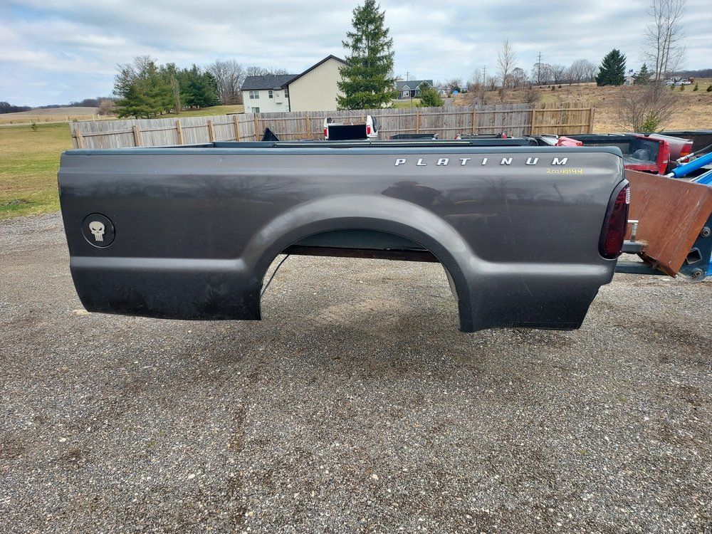 A gray truck bed is sitting on top of a gravel road.