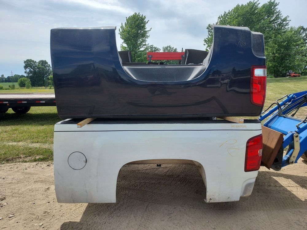A truck bed with a black tailgate is sitting on top of a white truck bed.