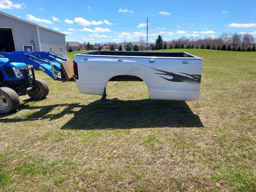 A white truck bed is sitting in a grassy field next to a blue tractor.