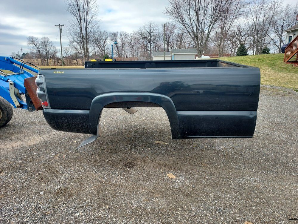 A black truck bed is sitting in a gravel lot next to a blue tractor.
