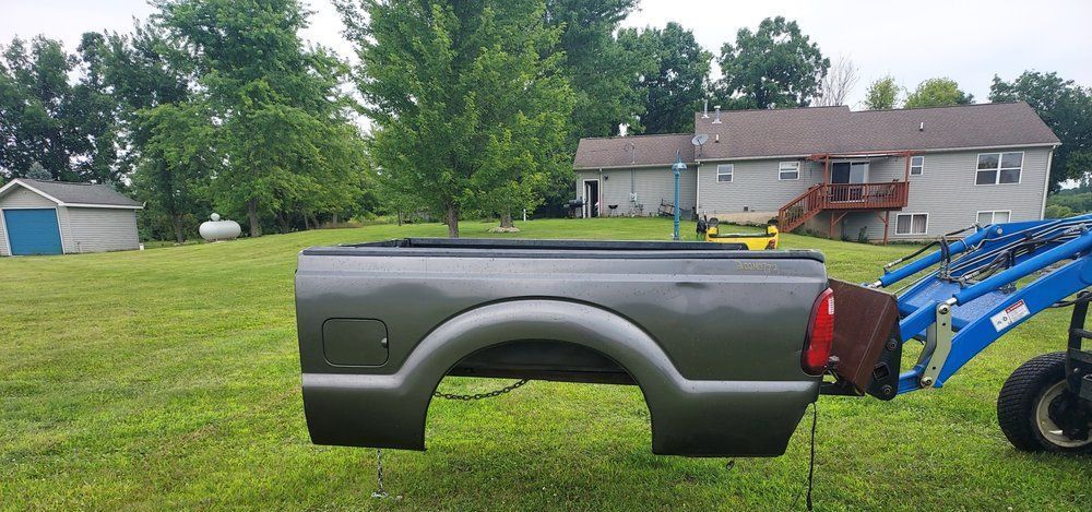 A truck bed is sitting in the grass next to a tractor.
