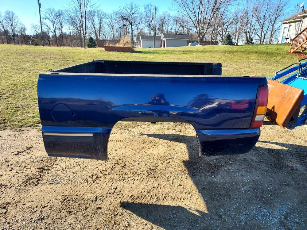 A blue truck bed is sitting on top of a dirt field.