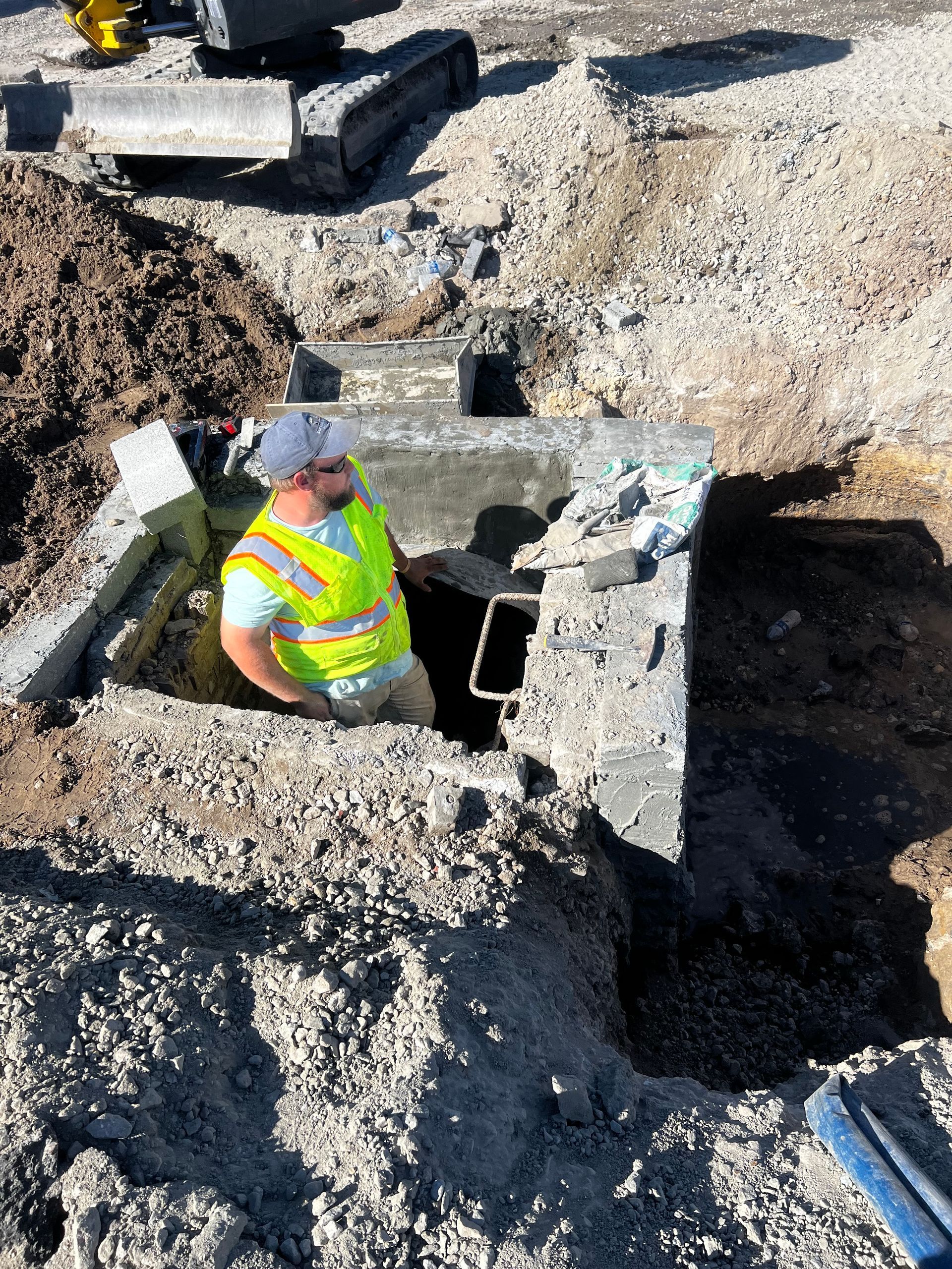 A man in a yellow vest is standing in a hole in the ground.