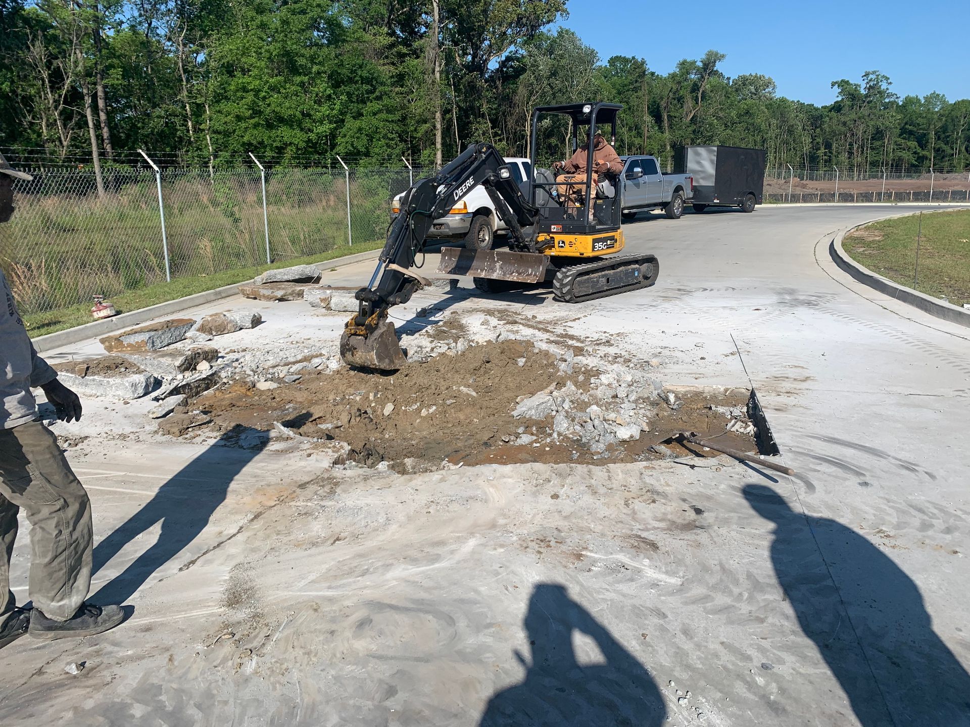 A man is standing next to a small excavator digging a hole in the ground.
