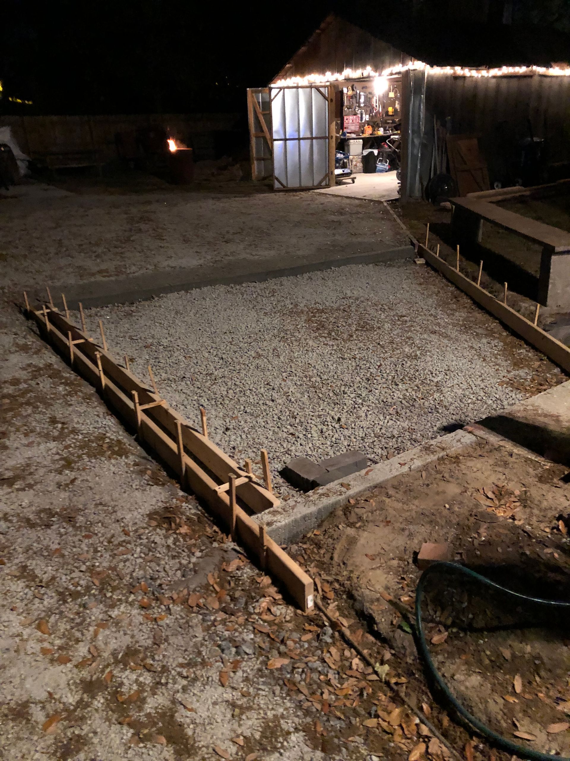 A concrete driveway is being built at night with a shed in the background.