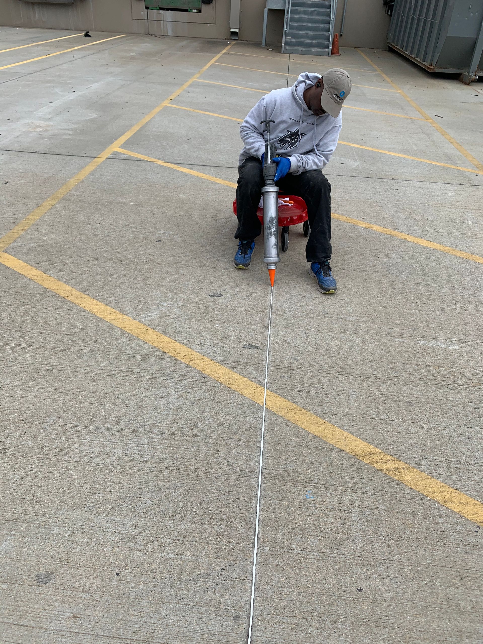 A man is sitting on the ground in a parking lot holding a tool.