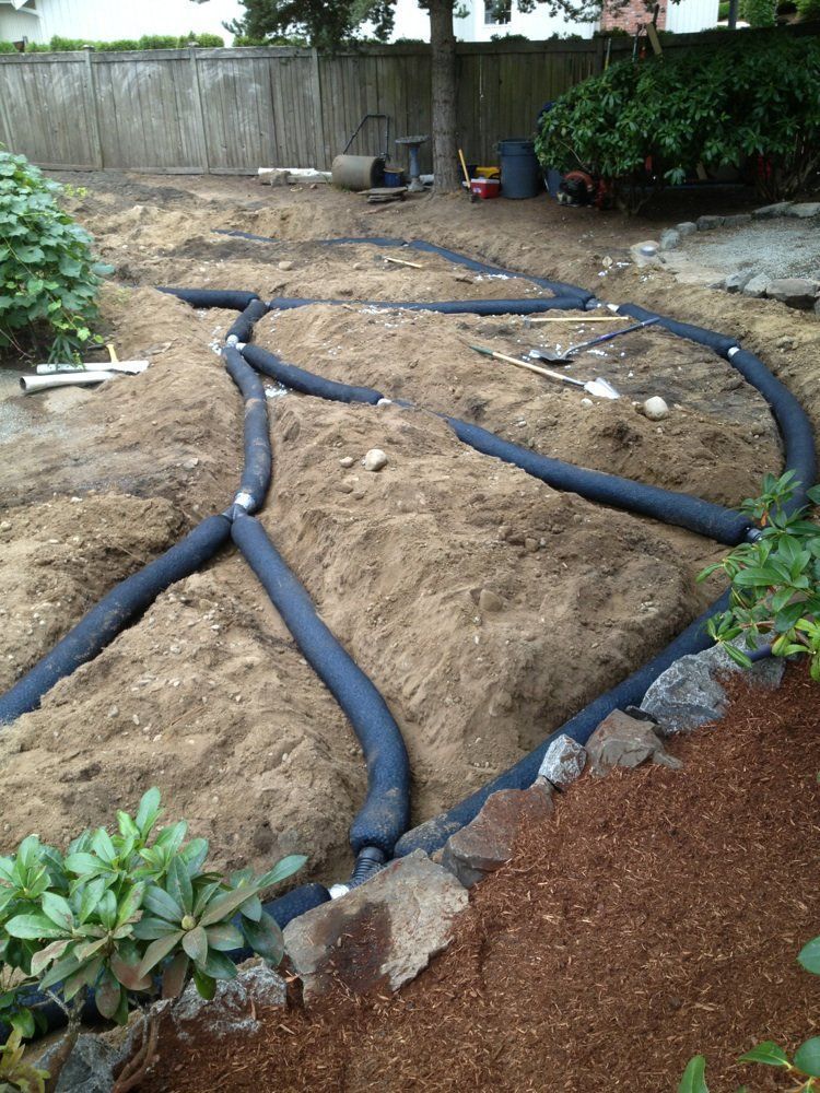 A bunch of pipes are laying in the dirt in a garden.