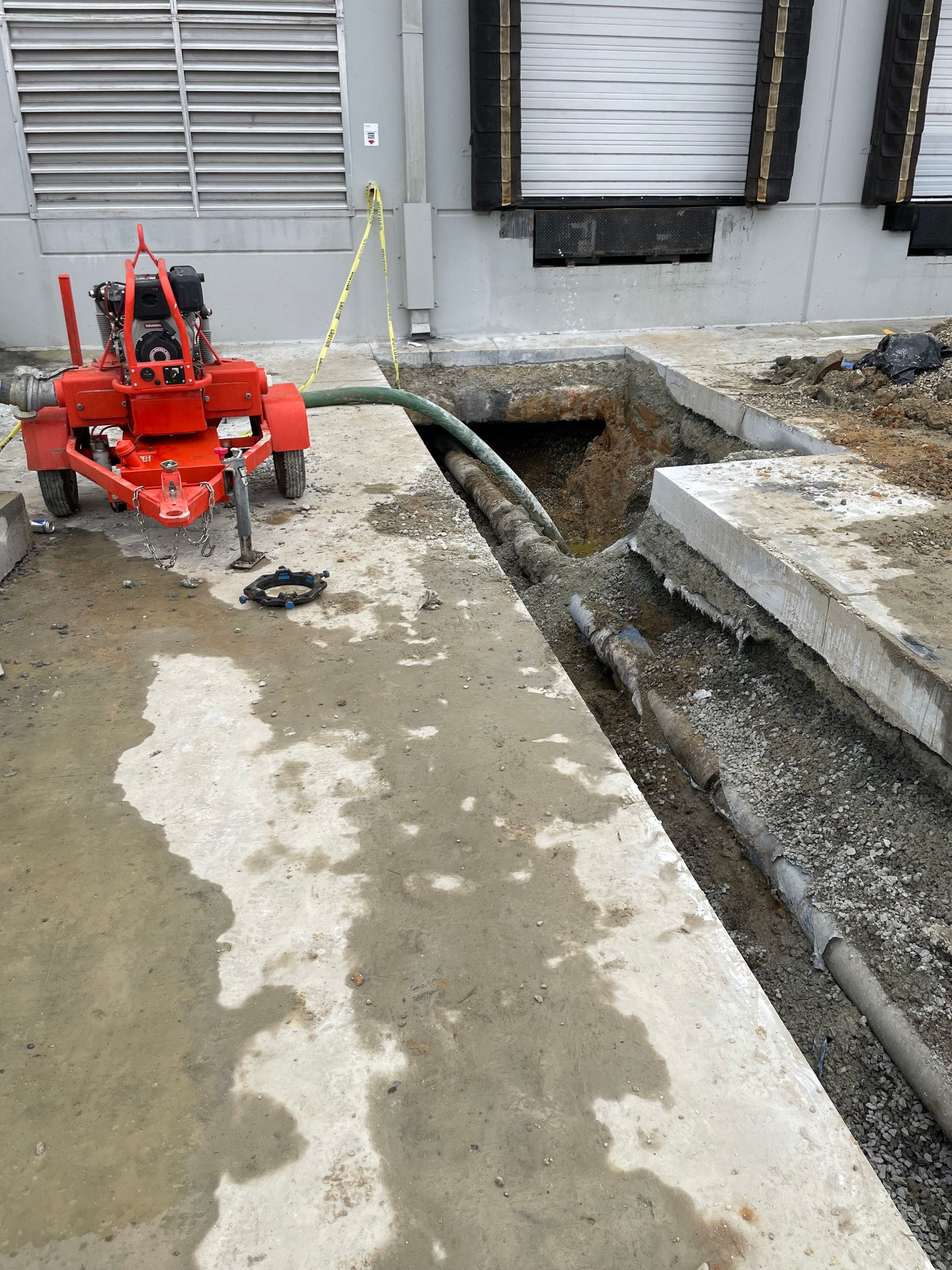 A red machine is sitting on a trailer next to a hole in the ground.
